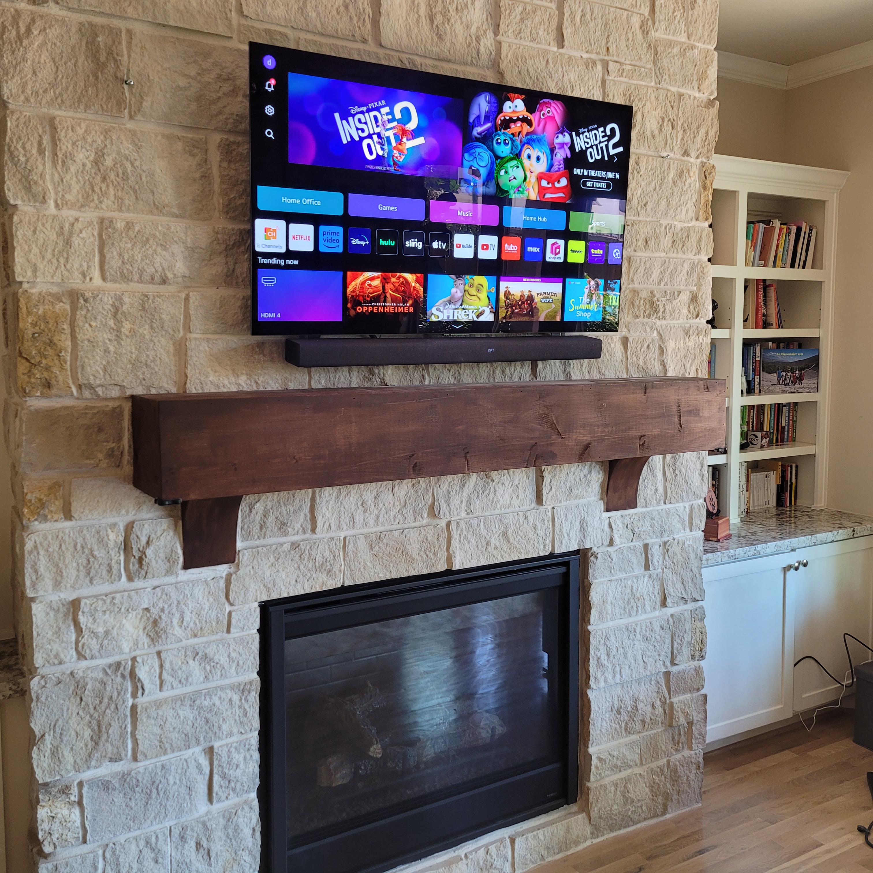 Large TV above Texas limestone fireplace with rustic wood beam mantle